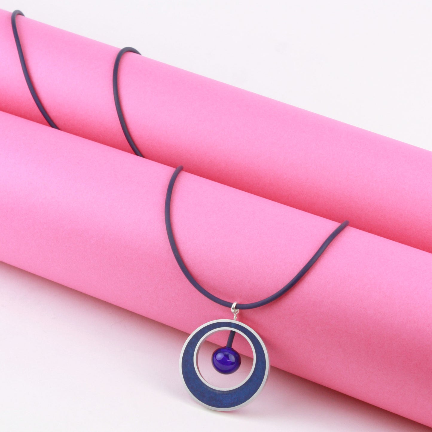 The Glory Necklace in Cobalt Blue, featuring a handcrafted pendant made from eco-resin, salvaged aluminum, and glossy blown glass, suspended on a fully adjustable silicone cord.