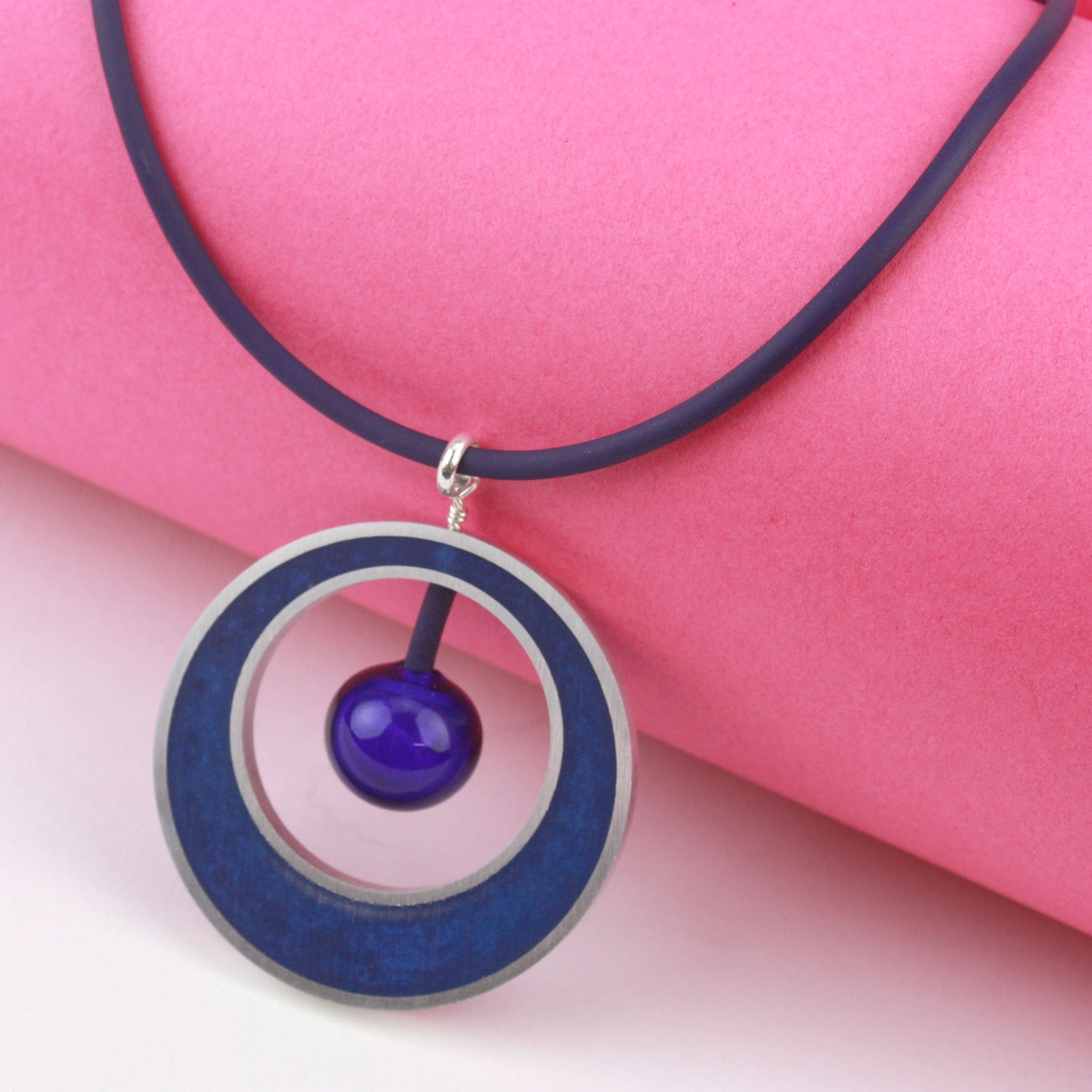 The Glory Necklace in Cobalt Blue, featuring a handcrafted pendant made from eco-resin, salvaged aluminum, and glossy blown glass, suspended on a fully adjustable silicone cord.