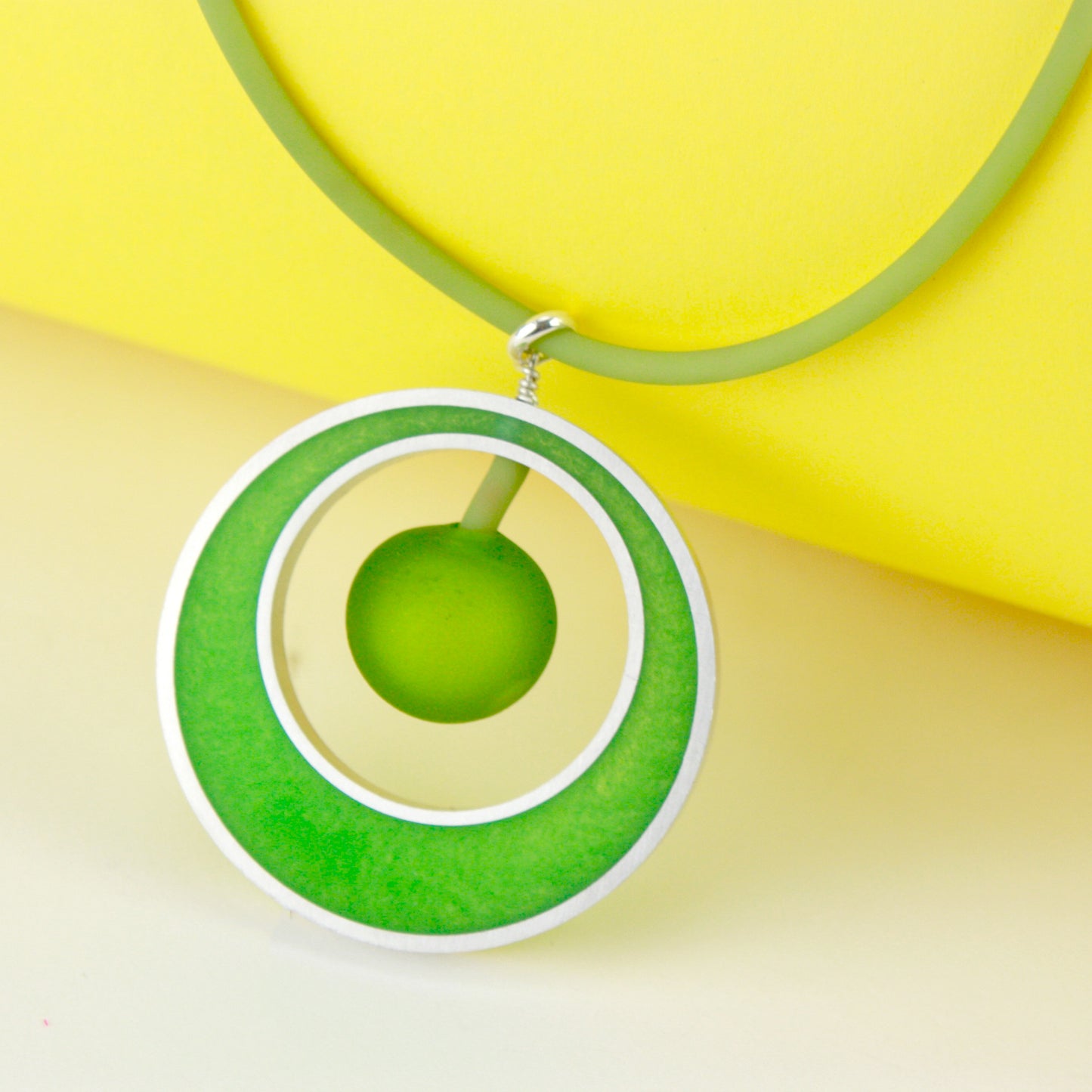 The Glory Necklace in Spring Green, featuring a handcrafted pendant made from eco-resin, salvaged aluminum, and frosted blown glass, suspended on a fully adjustable silicone cord.