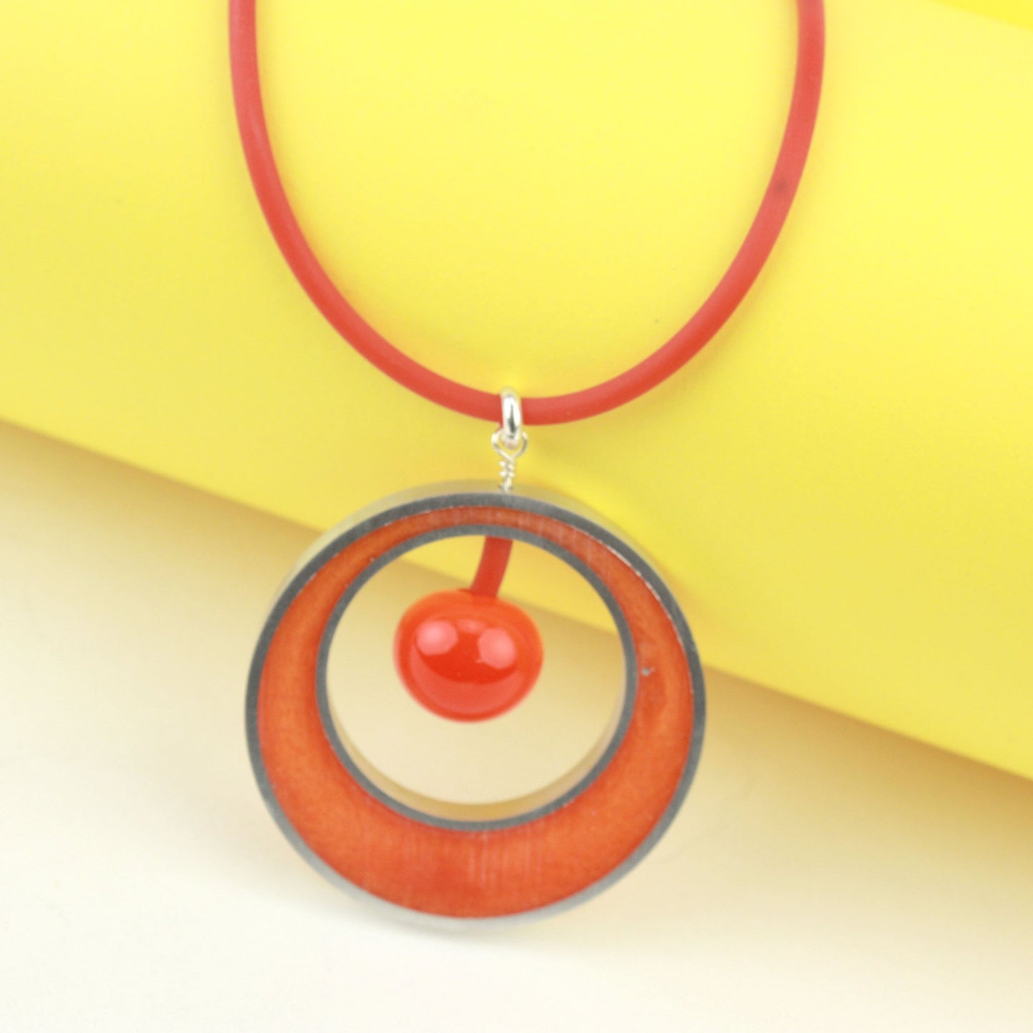 The Glory Necklace in Orange, featuring a handcrafted pendant made from eco-resin, salvaged aluminum, and glossy blown glass, suspended on a fully adjustable silicone cord.