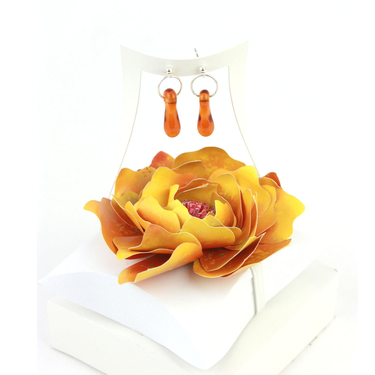 A pair of amber glass and sterling silver earrings displayed in a white gift box, adorned with a handcrafted golden-yellow paper flower.