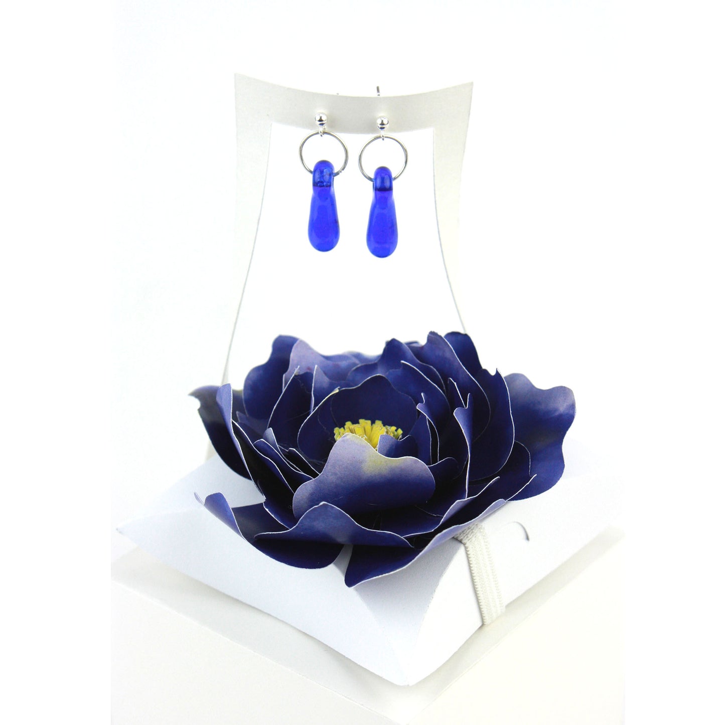 A pair of cobalt blue glass and sterling silver earrings displayed in a white gift box, decorated with a handcrafted deep blue paper flower.