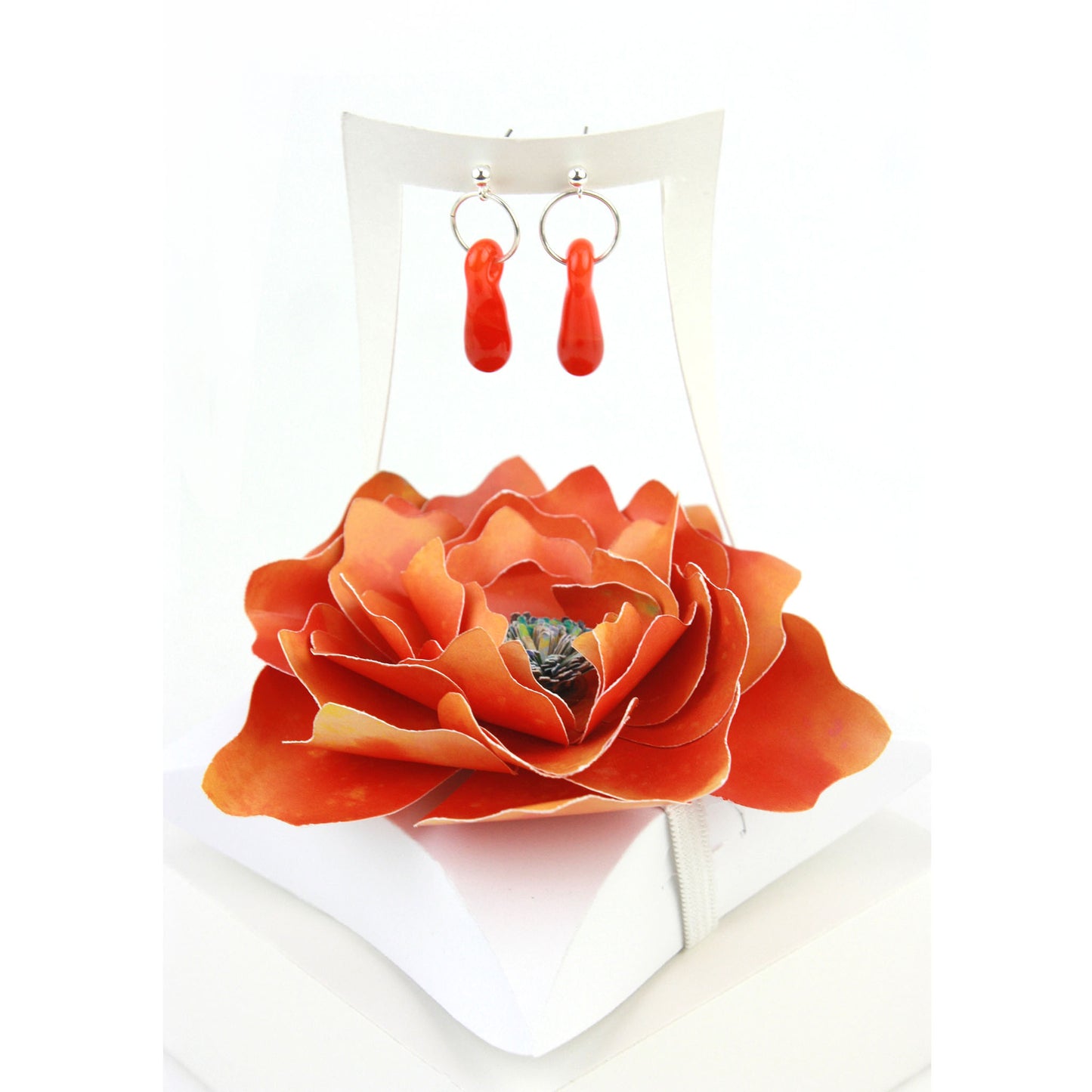 A pair of orange glass and sterling silver earrings displayed in a white gift box, adorned with a handcrafted orange paper flower.