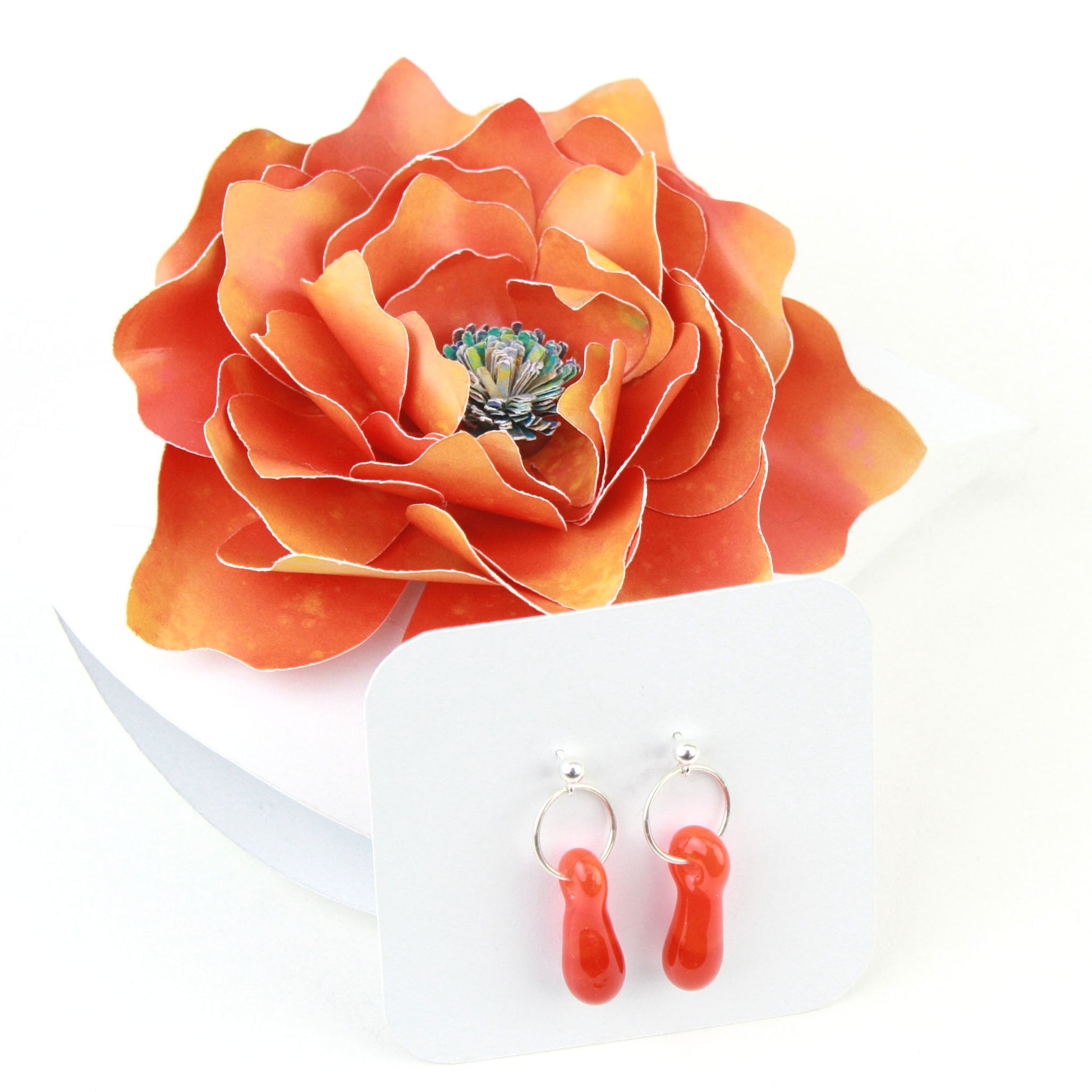 A pair of orange glass and sterling silver earrings displayed in a white gift box, adorned with a handcrafted orange paper flower.