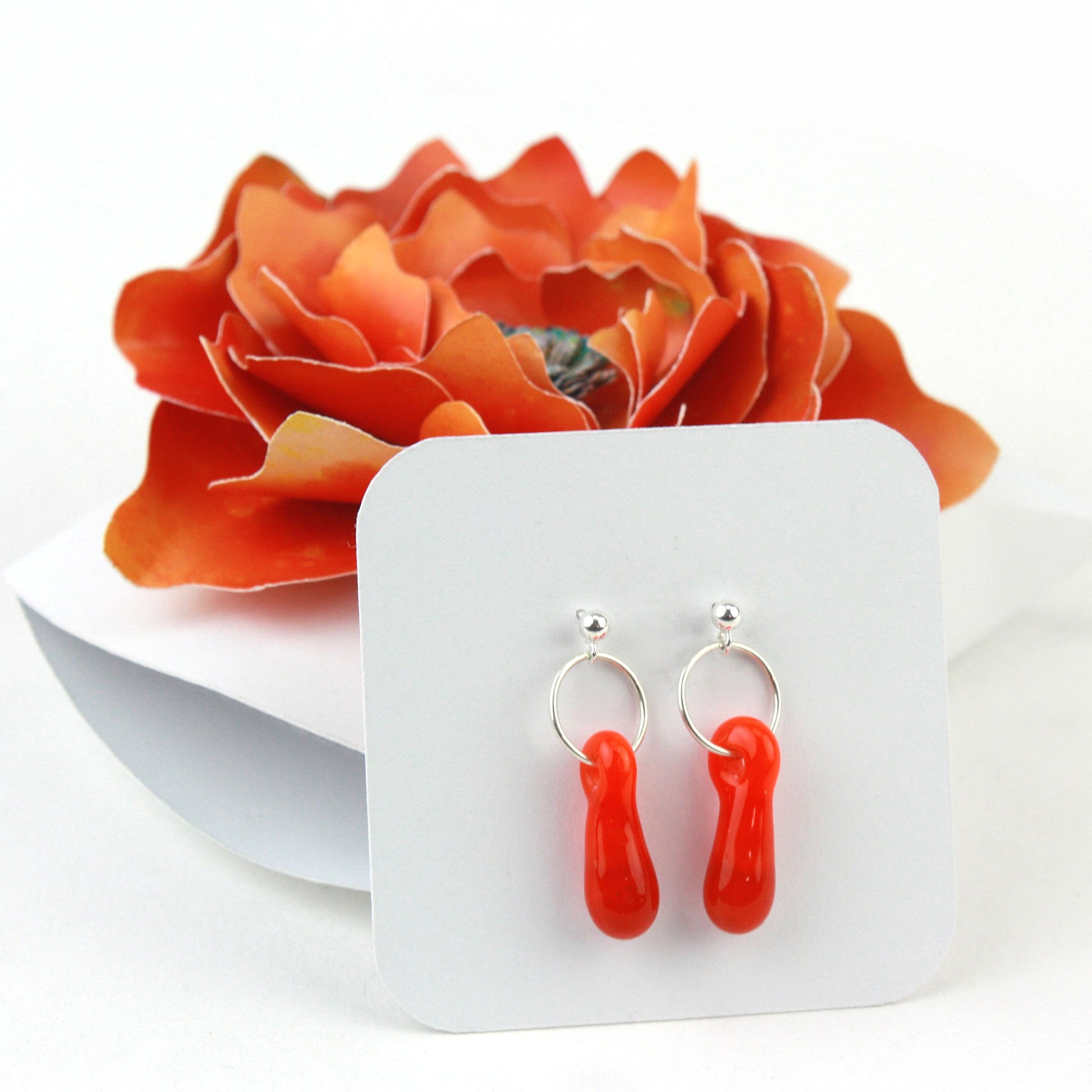 A pair of orange glass and sterling silver earrings displayed in a white gift box, adorned with a handcrafted orange paper flower.